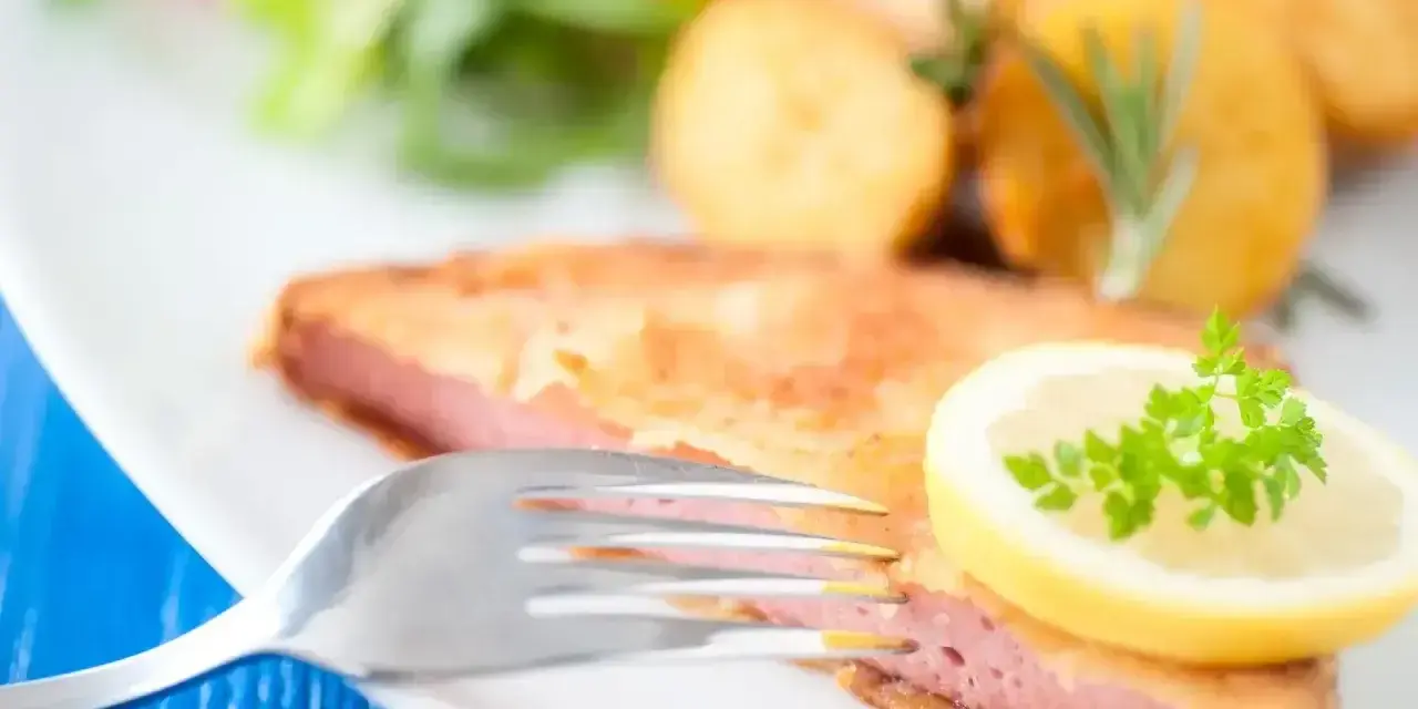 Smażony kotlet z mortadeli, podany z ziemniakami, sałatką i plasterkiem cytryny z natką pietruszki.