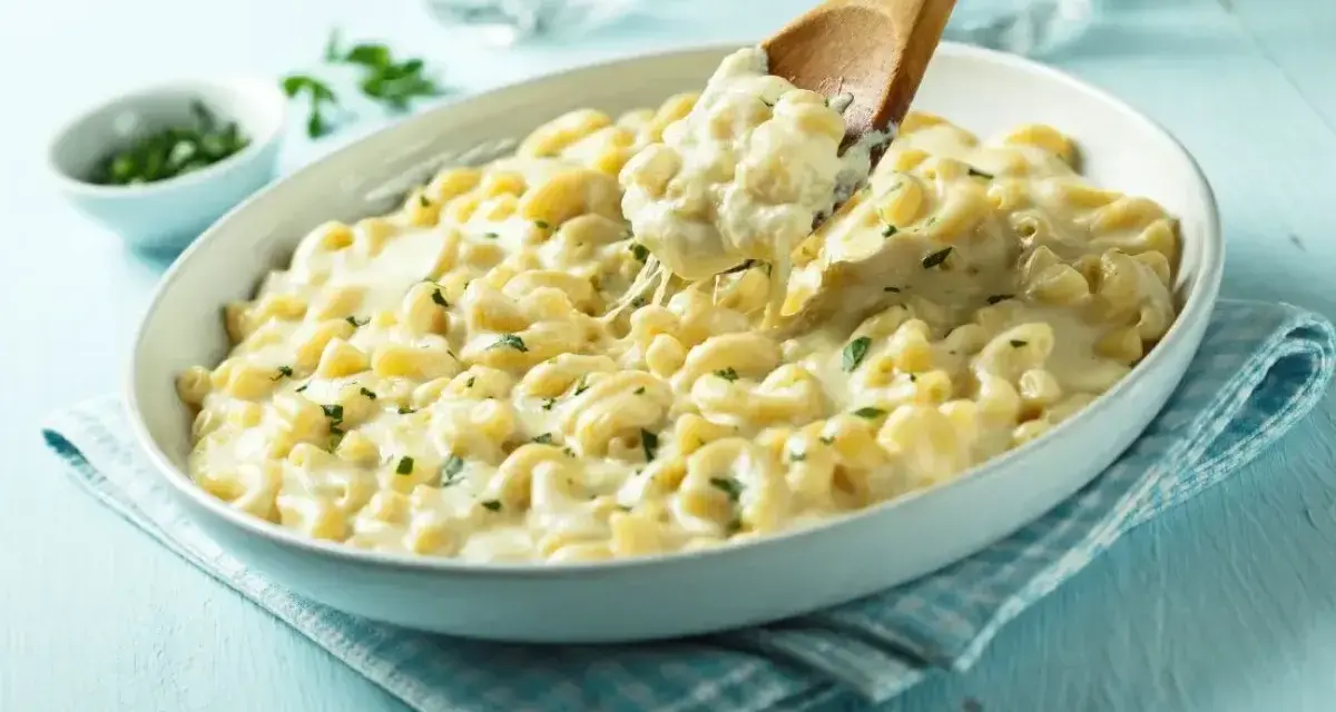 Kremowe makaronowe danie, idealne do przygotowania z przepisu na mac and cheese. Łyżka wydobywa porcję ciągnącego się sera.