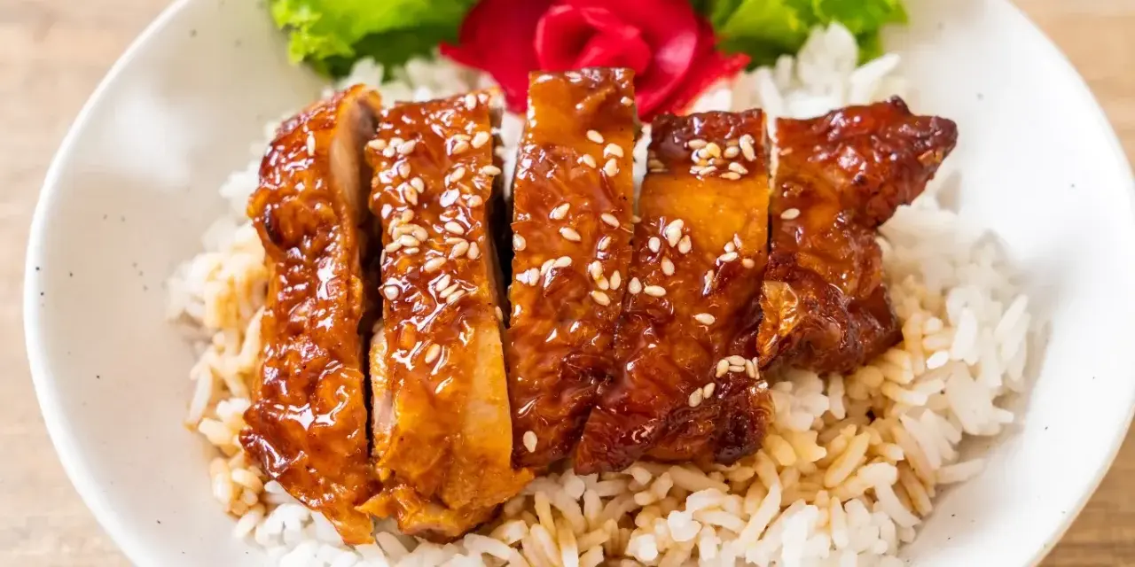 Pyszny kurczak w miodzie, polany sosem teriyaki i posypany sezamem, podany na ryżu z dodatkiem sałaty i marynowanego imbiru.