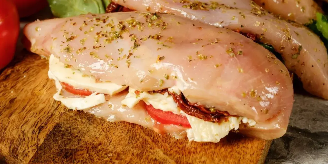 Nadziewana pierś z kurczaka z mozzarellą i suszonymi pomidorami, przyprawiona ziołami, gotowa do pieczenia.