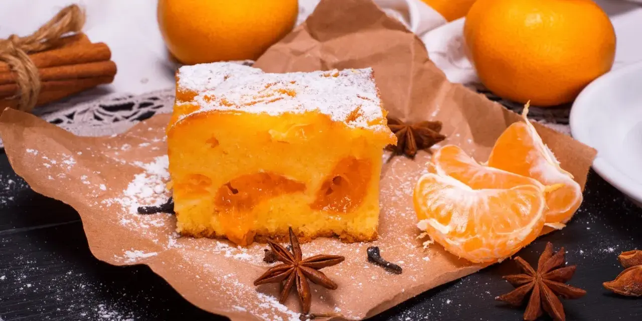 Puszyste ciasto z mandarynkami, posypane cukrem pudrem, obok świeże cząstki owoców i gwiazdki anyżu.