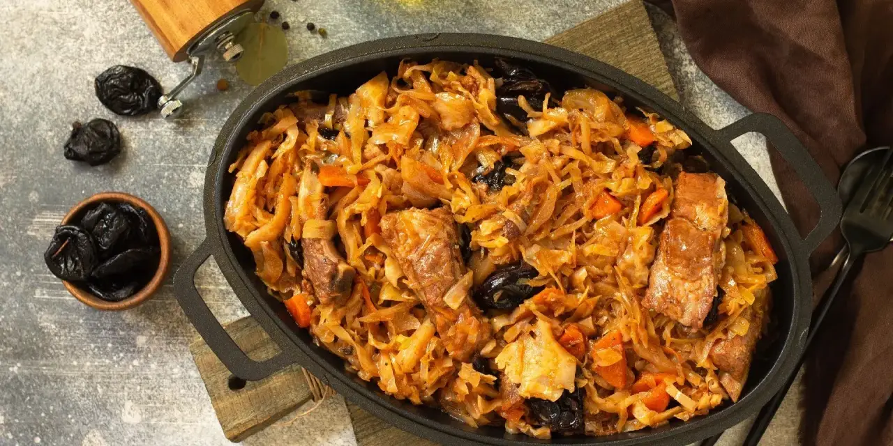 Pyszny bigos z kiszonej kapusty z kawałkami mięsa i śliwkami, podany w żeliwnym naczyniu.