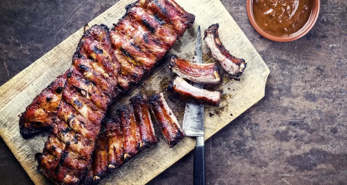 Soczyste żeberka w miodzie, grillowane do perfekcji, podane na desce z sosem.