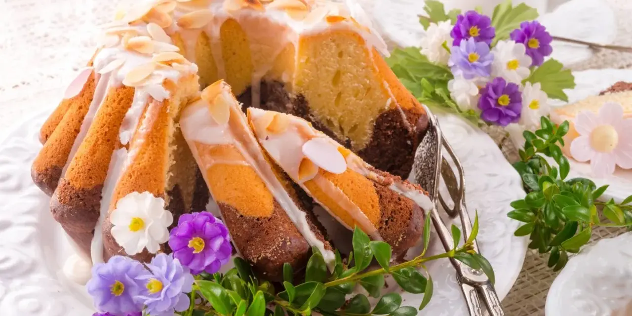 Modne ciasta na Wielkanoc: marmurkowa babka z lukrem i migdałami, ozdobiona wiosennymi kwiatami i zielenią.