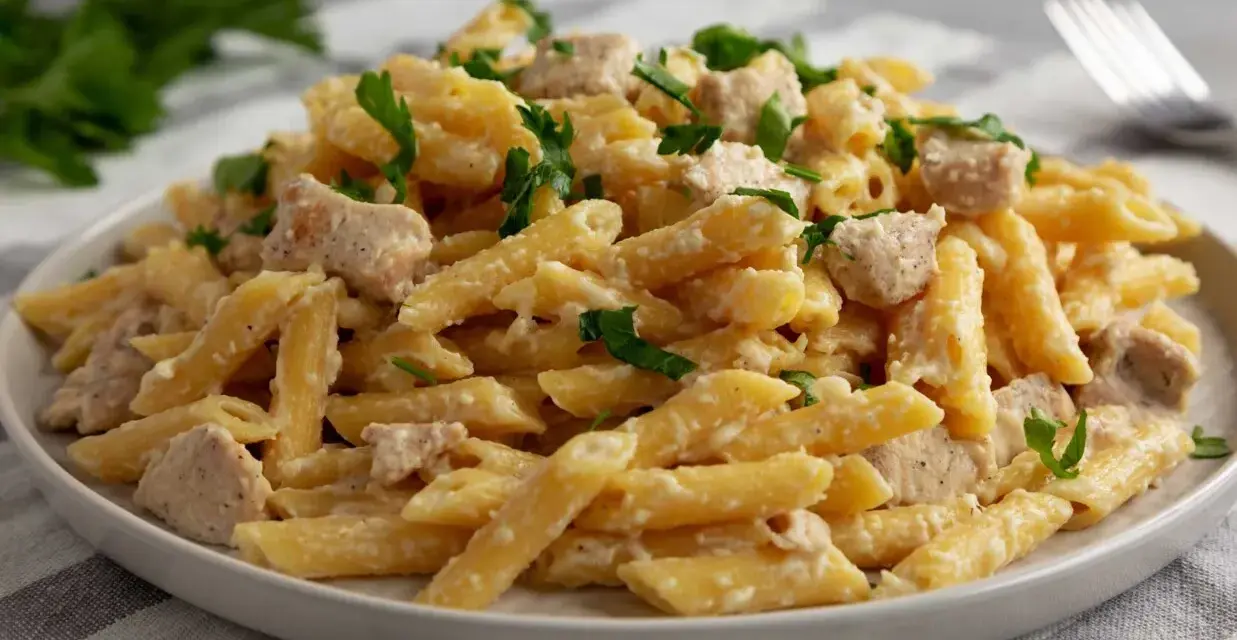 Penne z kremowym sosem i kawałkami indyka, posypane świeżą natką pietruszki. Pyszny makaron z indykiem na talerzu.
