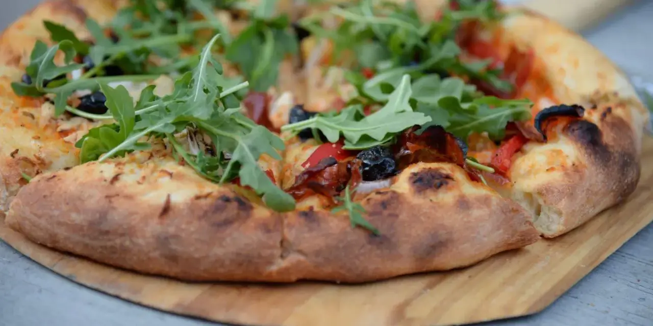 Pyszna pizza z rukolą i oliwkami na drewnianej desce. Proste ciasto na pizzę zawsze wychodzi, tworząc idealną bazę dla ulubionych dodatków.