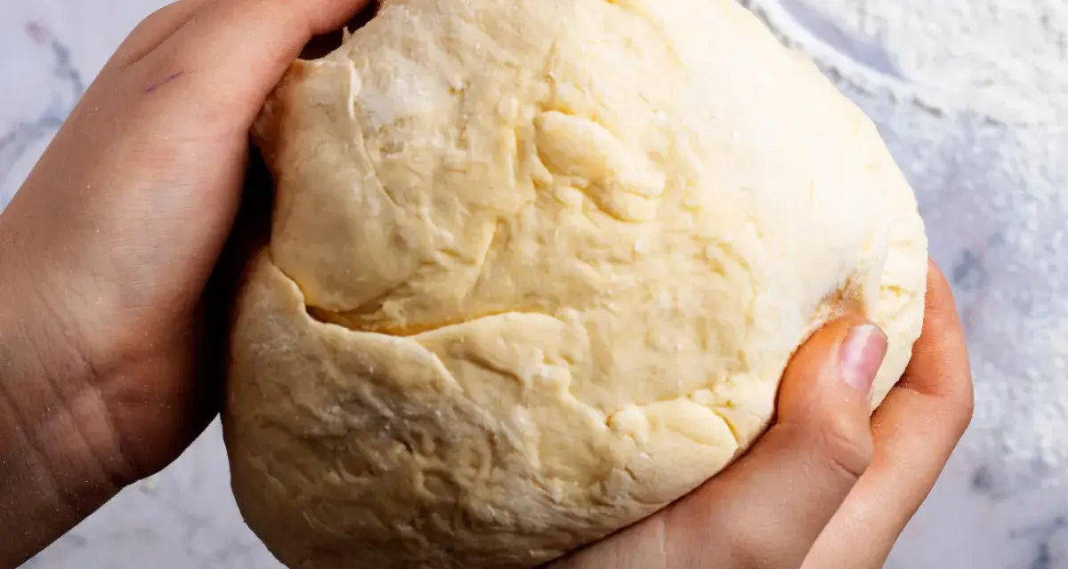 Dłonie formują puszyste ciasto drożdżowe na suchych drożdżach, gotowe do pieczenia.