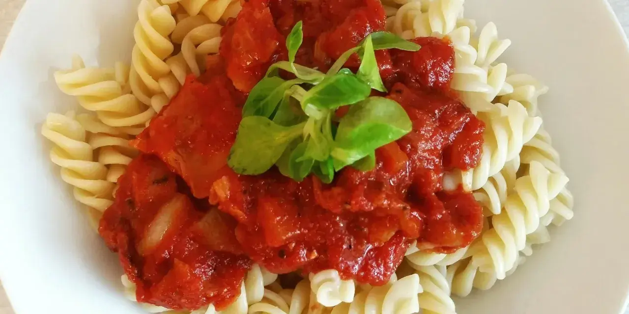 Fusilli z sosem pomidorowym i pomidorkami koktajlowymi, udekorowane świeżą zieleniną. Pyszne danie gotowe w kilka minut.