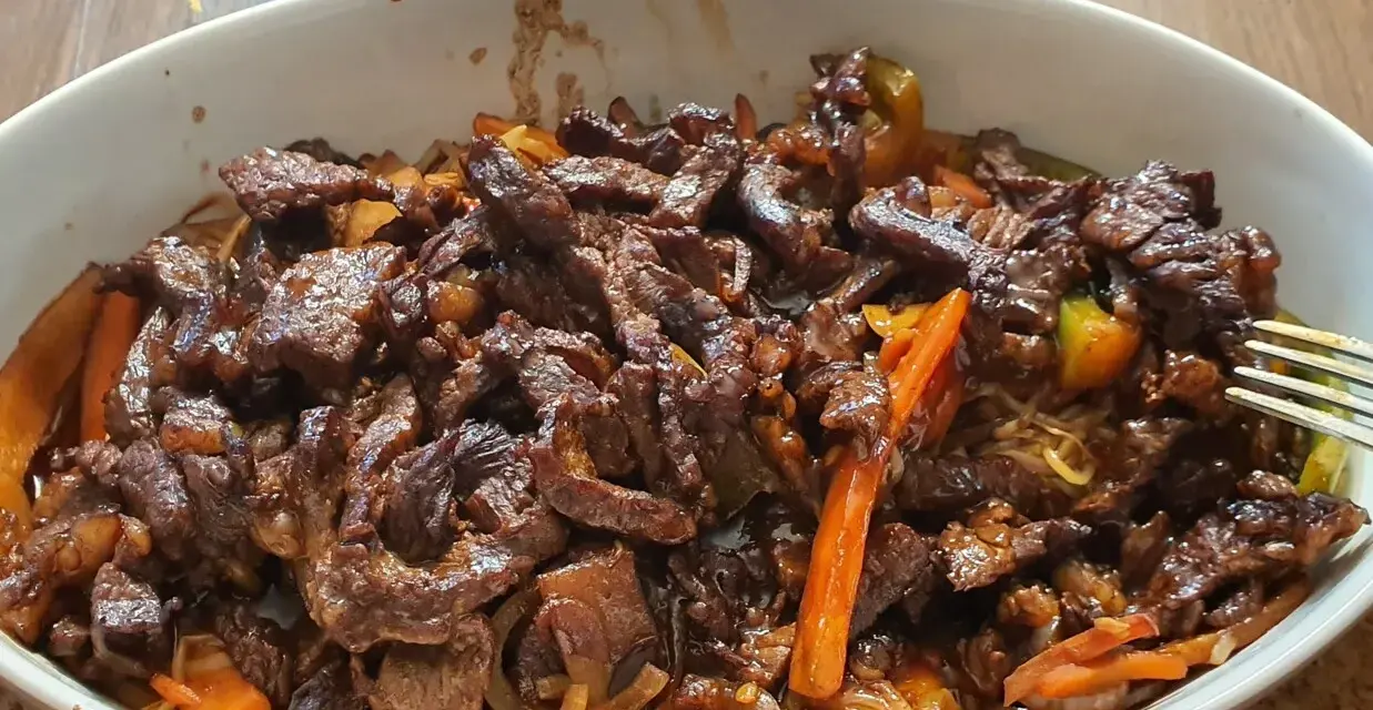 Pyszne wołowina stir fry z warzywami i makaronem, podane w białej misce.