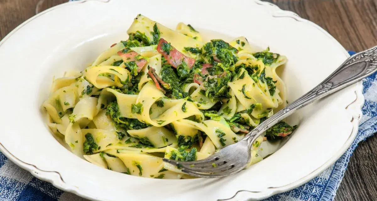 Pappardelle z boczkiem i szpinakiem, danie pełne smaku, podane na talerzu z widelcem.