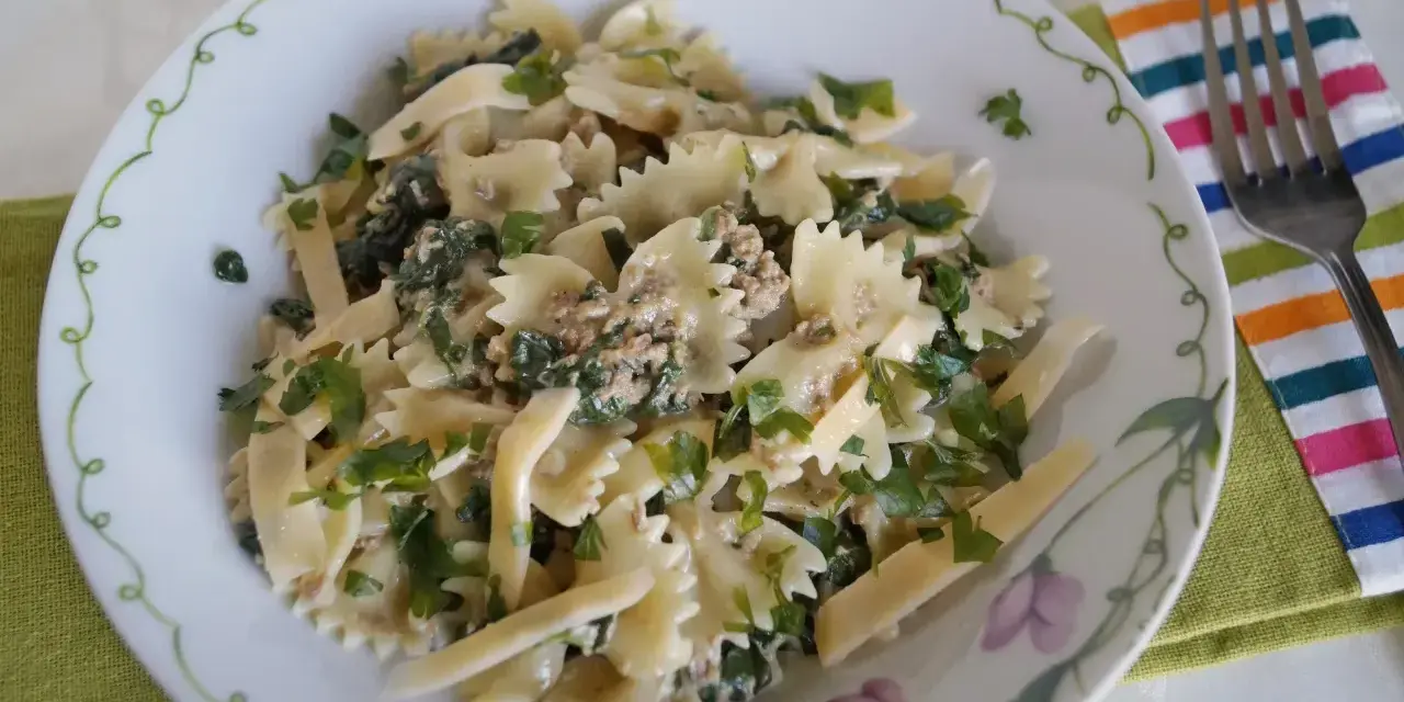 Pyszny makaron z pesto i tuńczykiem, posypany świeżą natką pietruszki, podany na talerzu z ozdobnym brzegiem.