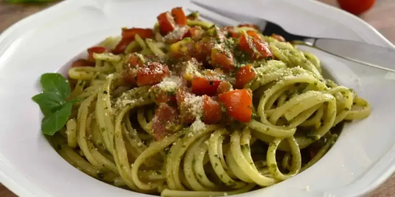 Pyszny makaron z pesto, pomidorkami i parmezanem, udekorowany listkiem bazylii. Idealny na szybki obiad.