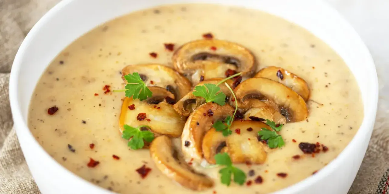 Aksamitny zupa krem z pieczarek, udekorowana plasterkami pieczarek, natką pietruszki i płatkami chili. Idealna na chłodne dni.