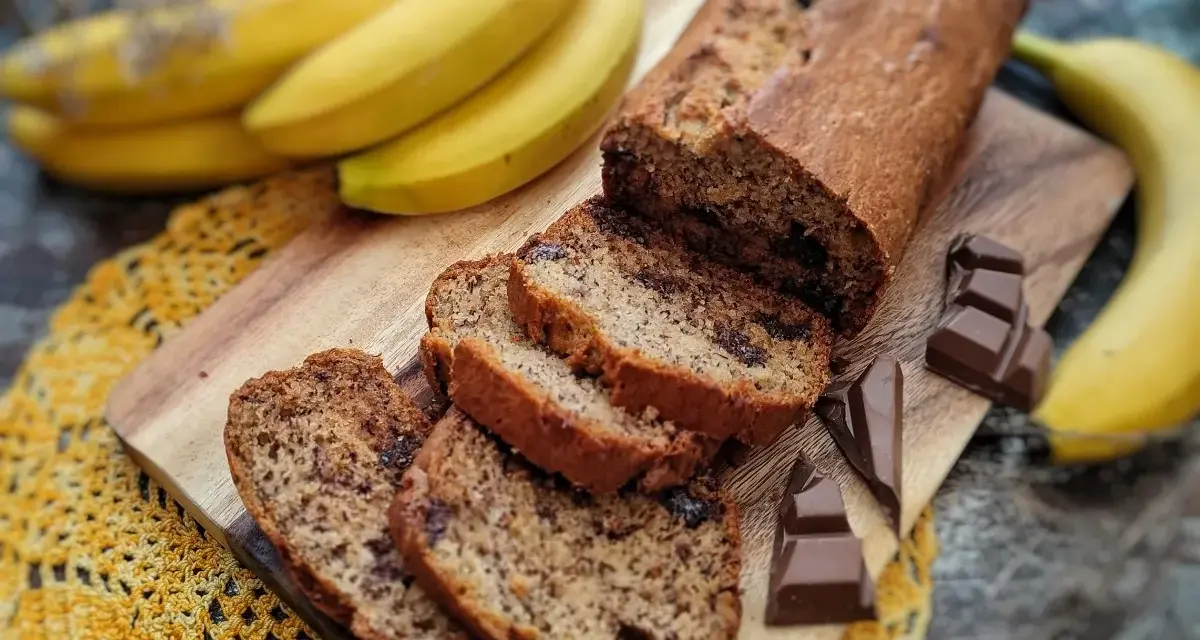 Pyszny chlebek bananowy z czekoladą, pokrojony na kromki, obok świeże banany i kawałki czekolady.