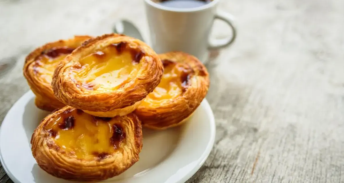 Na talerzyku leżą trzy chrupiące pastéis de nata, obok filiżanka kawy. Idealny poranek.