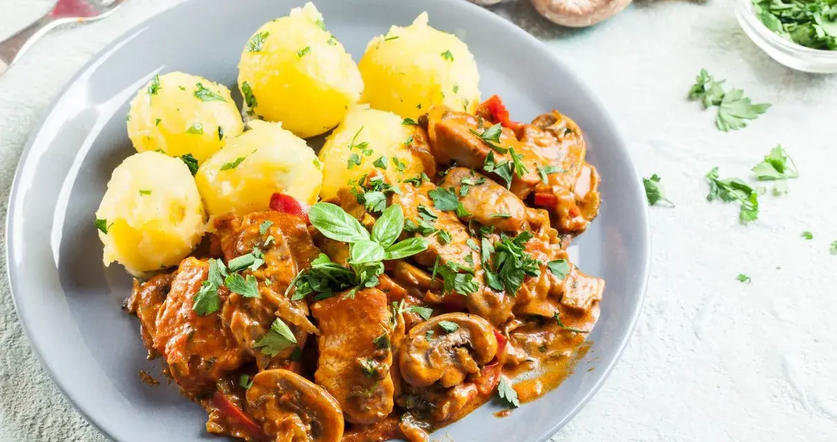 Gulasz drobiowy z pieczarkami i ziemniakami na talerzu, ozdobiony natką pietruszki.