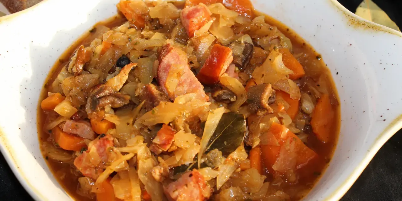 Pyszny bigos ze słodkiej kapusty z kiełbasą i marchewką, podany w białej misie.