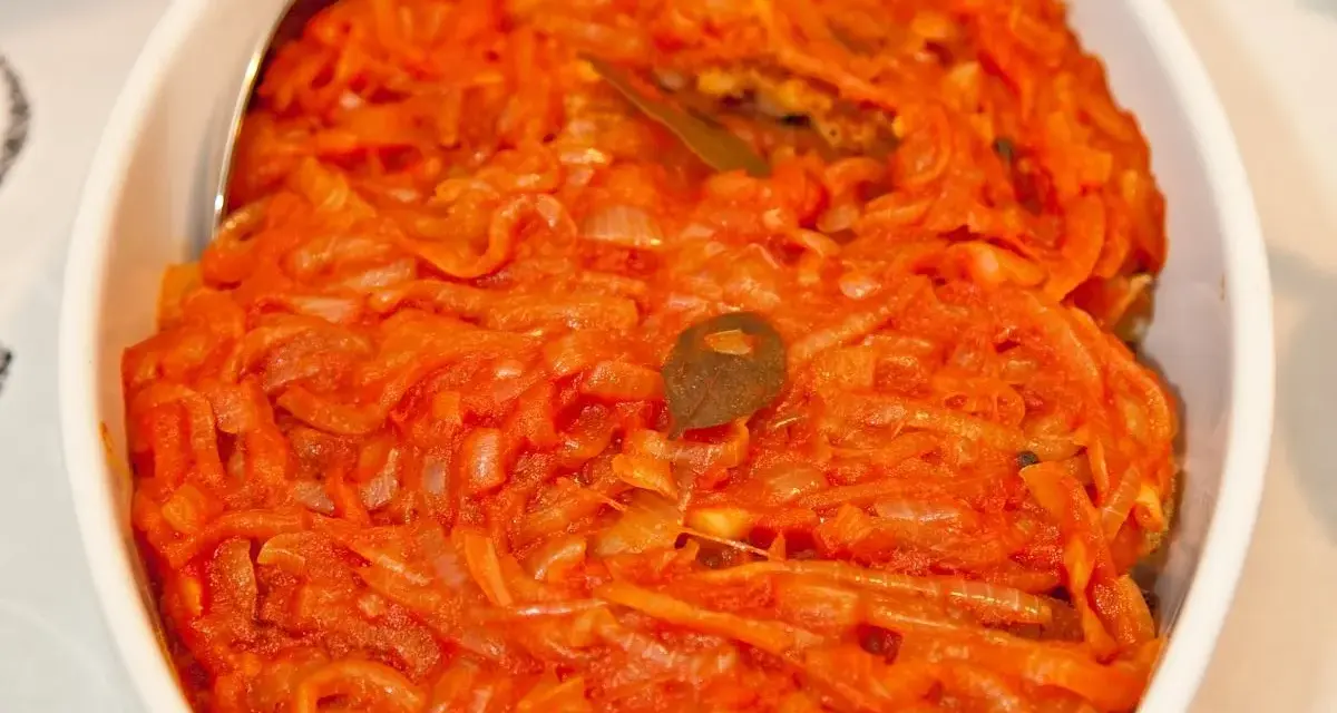 Ryba po grecku Ani Gotuje w sosie pomidorowo-cebulowym, podana w białej misie.