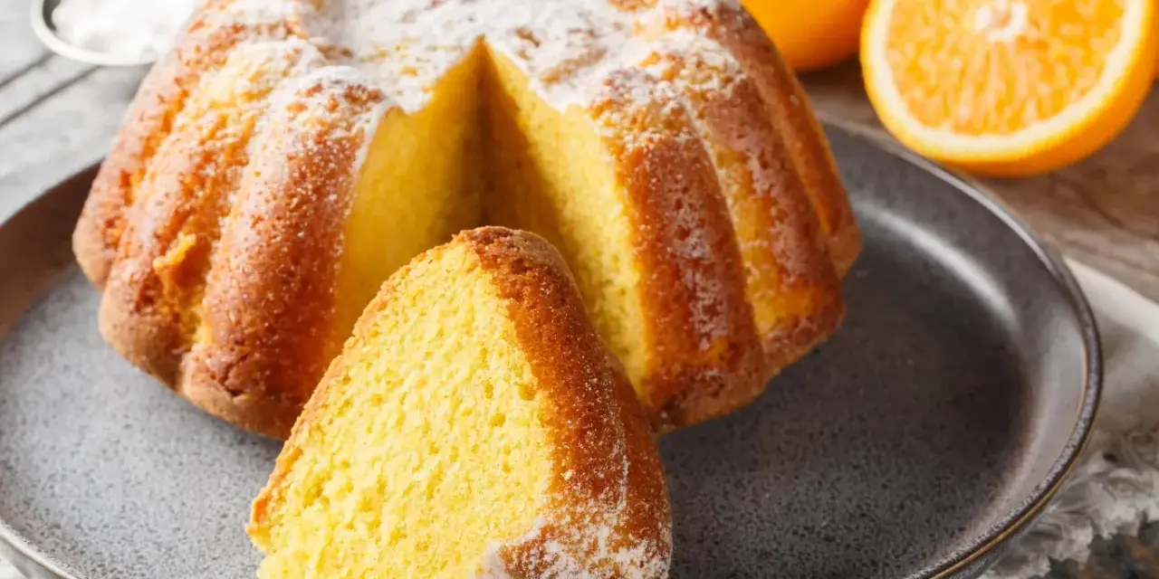 Puszysta babka na oleju, oprószona cukrem pudrem, z pomarańczami w tle. Idealna na niedzielne popołudnie.
