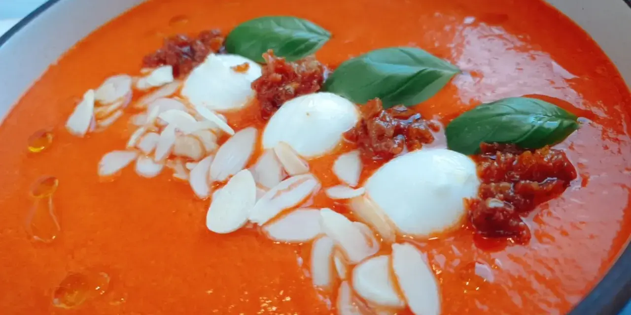 Aksamitny krem z pieczonej papryki z kulkami mozzarelli, suszonymi pomidorami, płatkami migdałów i listkami bazylii.