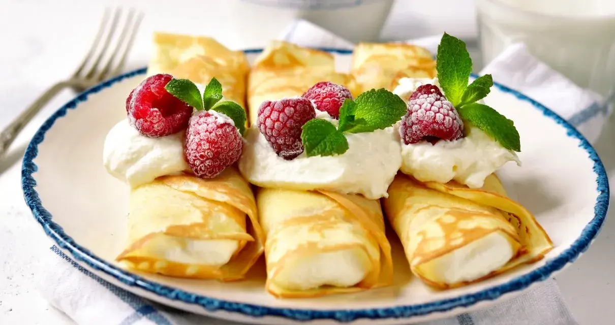 Rolowane naleśniki z mascarpone, udekorowane malinami i miętą, wyglądają apetycznie.