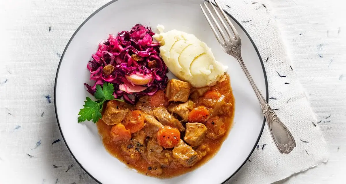 Gulasz wieprzowy z warzywami, podany z purée ziemniaczanym i czerwoną kapustą. Pyszne danie obiadowe.