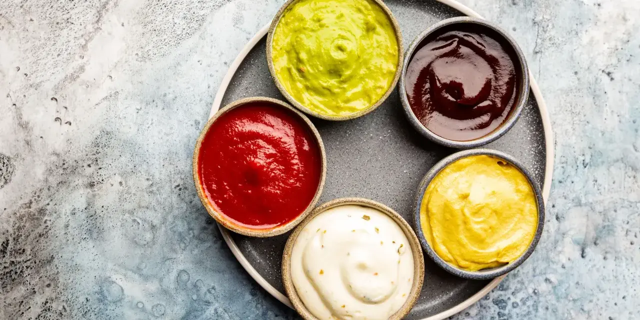 Sześć miseczek z sosami: zielony guacamole, czerwony ketchup, ciemny barbecue, żółta musztarda i biały majonez. Idealne do dań, gdy zastanawiasz się, jak zrobić sos.