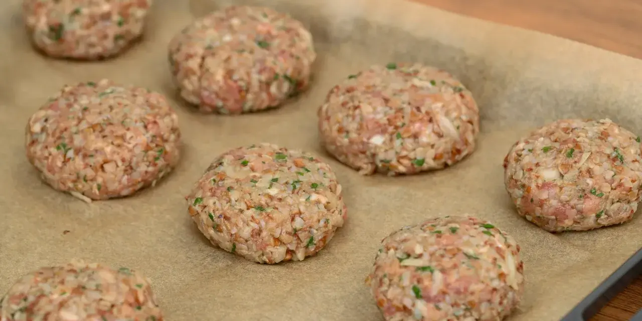 Surowe burgery z piekarnika, przygotowane z mielonego mięsa i kaszy, leżą na papierze do pieczenia.
