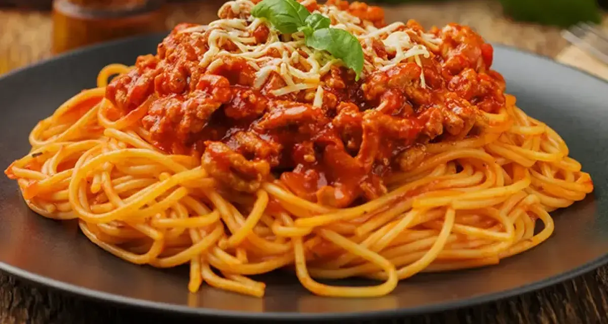 Pyszne spaghetti z mięsem mielonym, polane sosem pomidorowym i posypane startym serem, ozdobione listkiem bazylii.