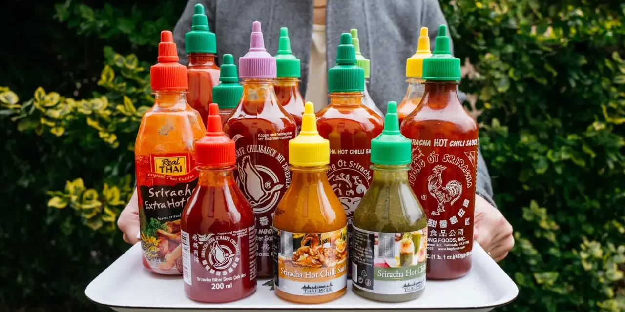Taca z wieloma butelkami sosu Sriracha o różnych kolorach nakrętek.