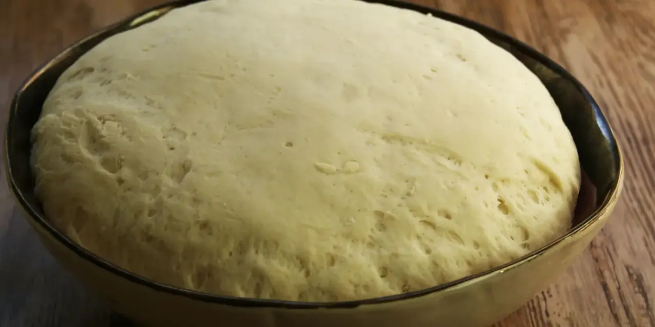 Puszyste ciasto na pizzę wyrosło w misce, gotowe do dalszej obróbki.