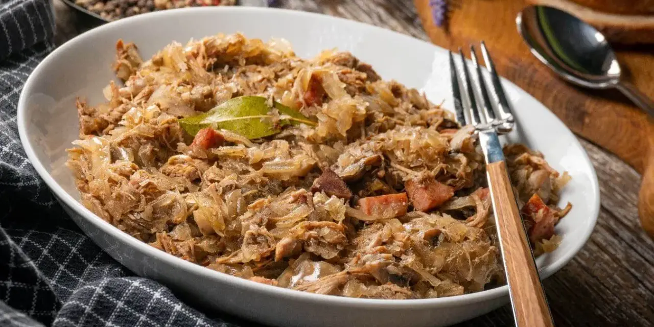 Pyszny bigos w białej misce, z widelcem. Zastanawiasz się, ile może stać bigos w lodówce? Nawet kilka dni, a smakuje coraz lepiej!