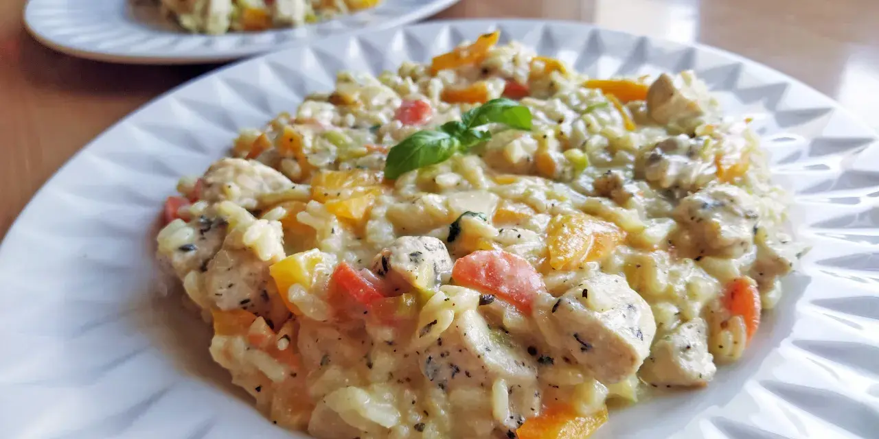 Pyszne risotto z kurczakiem i kolorowymi warzywami, udekorowane listkiem bazylii. Idealne na obiad.