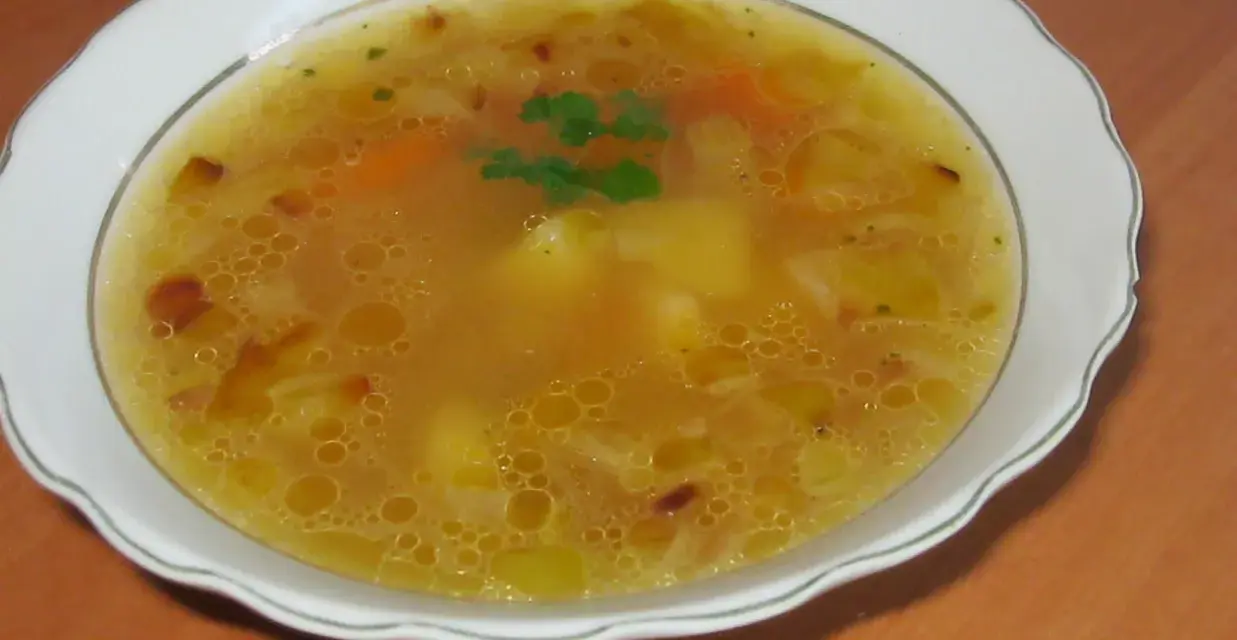 Prosta zupa cebulowa z ziemniakami, z kawałkami marchewki i natką pietruszki, podana w białej misce.