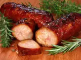 Soczysta kiełbasa pieczona w piekarniku, skropiona błyszczącym sosem, z gałązkami rozmarynu i ziarnami pieprzu.