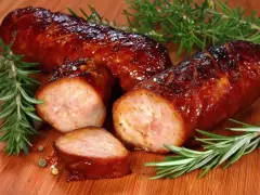 Soczysta kiełbasa pieczona w piekarniku, skropiona błyszczącym sosem, z gałązkami rozmarynu i ziarnami pieprzu.