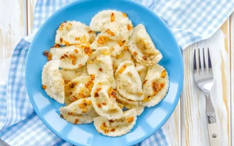 Pyszne pierogi z soczewicą czerwoną, posypane skwarkami i pieprzem, na niebieskim talerzu.
