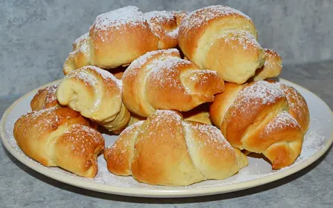 Stos świeżo upieczonych rogalików z czekoladą, posypanych cukrem pudrem, na talerzu.