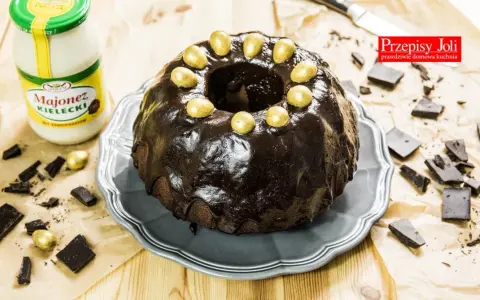 Babka majonezowa z przepisów Joli, polana czekoladą i ozdobiona złotymi jajeczkami. Obok słoik majonezu i kawałki czekolady.