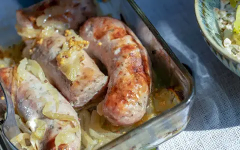 Biała kiełbasa pieczona z cebulką i musztardą w szklanym naczyniu. Apetyczny zapach unosi się w powietrzu.