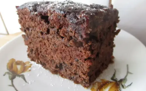 Wilgotne ciasto czekoladowe z dżemem porzeczkowym, posypane cukrem pudrem, na talerzyku z motywem kwiatowym.