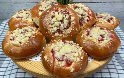 Pyszne, złociste drożdżówki z kruszonką i owocowym nadzieniem, ułożone na drewnianej desce.