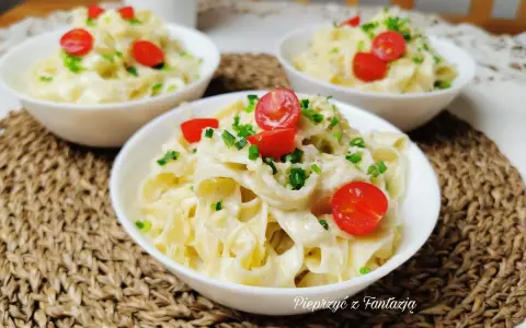 Pyszny makaron tagliatelle w kremowym sosie 4 sery, udekorowany pomidorkami koktajlowymi i szczypiorkiem. Idealny na szybki obiad.