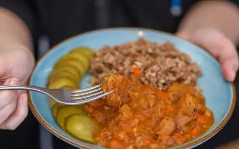 Pyszny gulasz z kaszą gryczaną i ogórkami kiszonymi na talerzu. Widok z bliska na kawałek mięsa nabierany widelcem.
