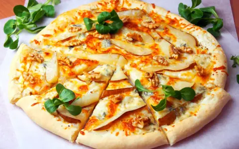 Apetyczna pizza z gruszką i gorgonzolą, ozdobiona orzechami włoskimi i świeżą rukolą. Idealna na wyjątkowy wieczór.