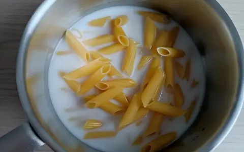 Makaron penne gotuje się w mleku w metalowym garnku.