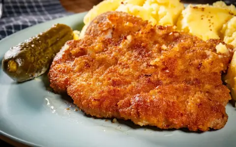 Chrupiące kotlety z karkówki, purée ziemniaczane i ogórek kiszony na talerzu.
