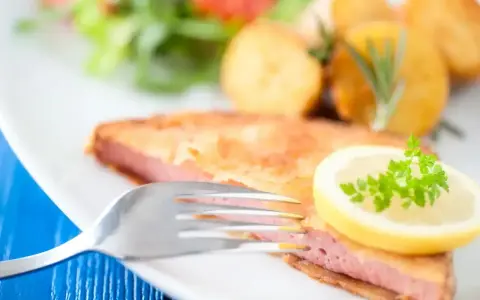 Smażony kotlet z mortadeli, podany z ziemniakami, sałatką i plasterkiem cytryny z natką pietruszki.