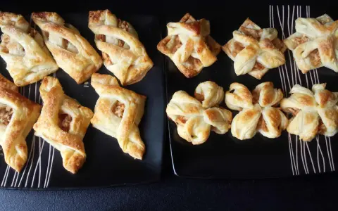 Słodkie przekąski z ciasta francuskiego z jabłkami, posypane cukrem. Różne kształty, niektóre przypominają gwiazdki.