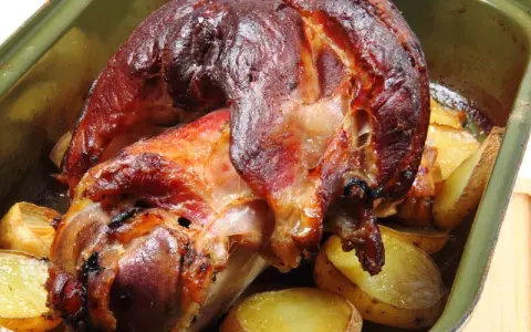 Pieczona golonka w zielonej brytfance, otoczona ziemniakami. Idealna marynata do golonki sprawiła, że skórka jest chrupiąca.